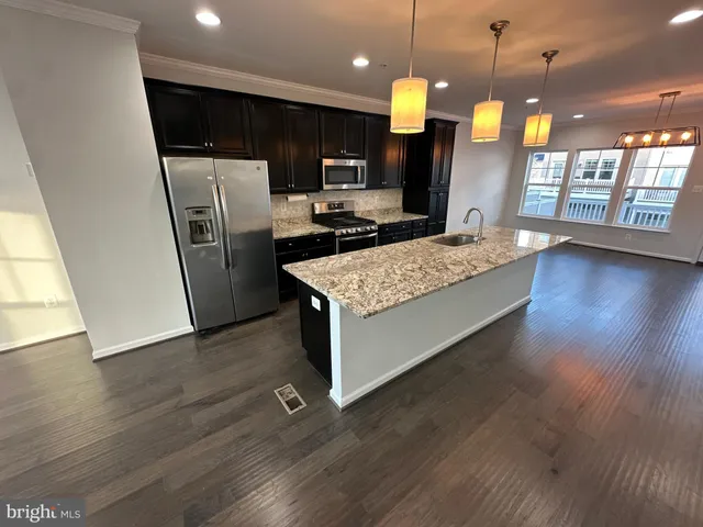 a kitchen with stainless steel appliances granite countertop a refrigerator a sink dishwasher a stove and a dining table with wooden floor