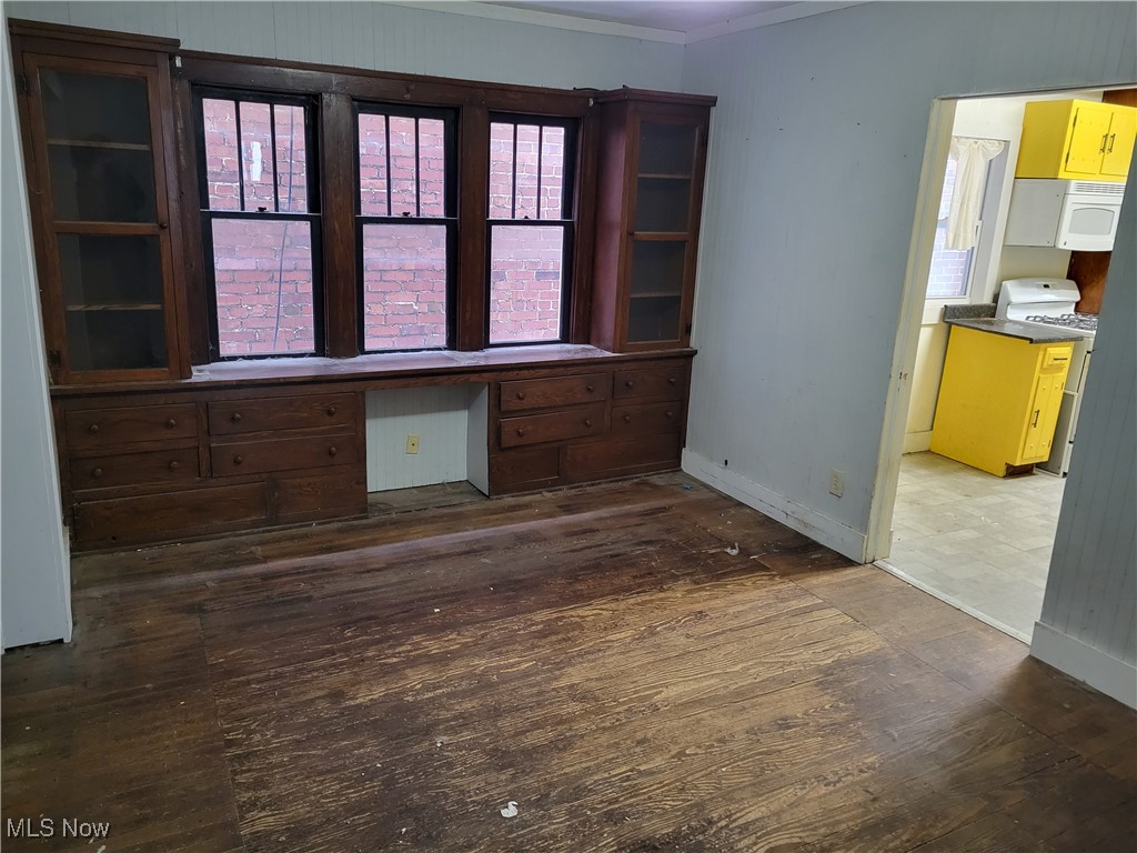 Unfurnished living room with built in desk, dark wood-type flooring, and crown molding