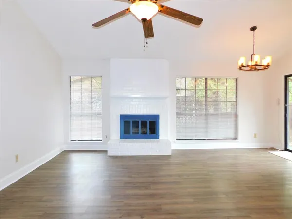 an empty room with wooden floor fan and windows