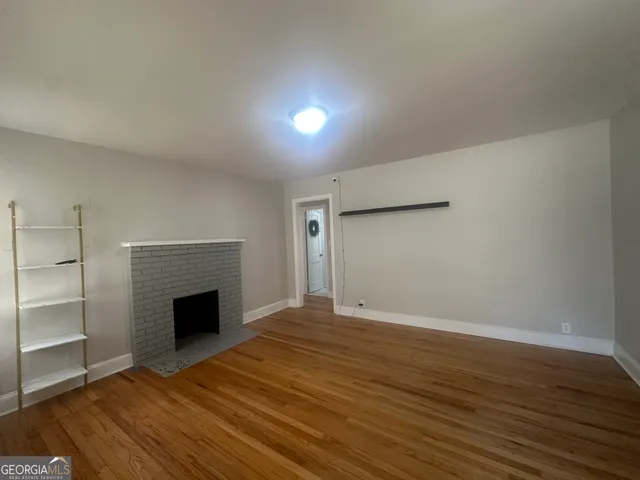 a view of an empty room with wooden floor fireplace and a window
