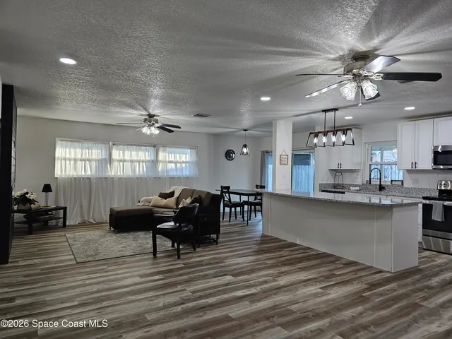 a kitchen with stainless steel appliances kitchen island granite countertop a refrigerator a sink dishwasher a stove and a dining table with wooden floor