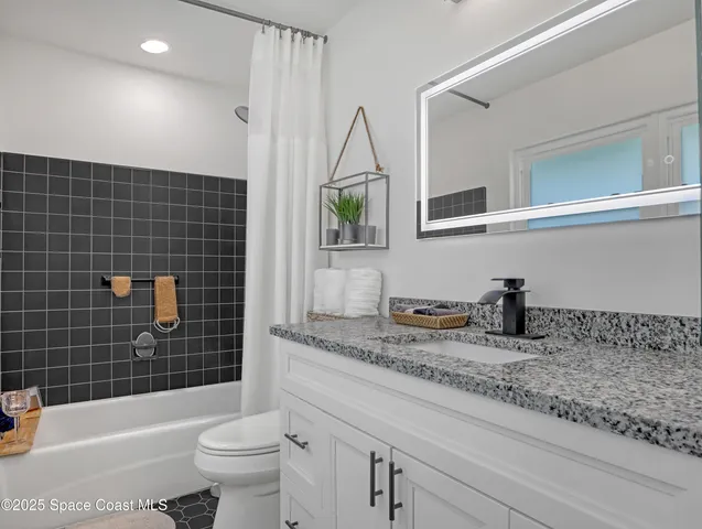 a bathroom with a granite countertop sink a toilet a mirror a bathtub and shower