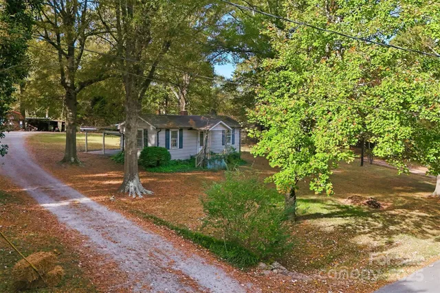 a view of house in front of a yard with potted plants and large trees