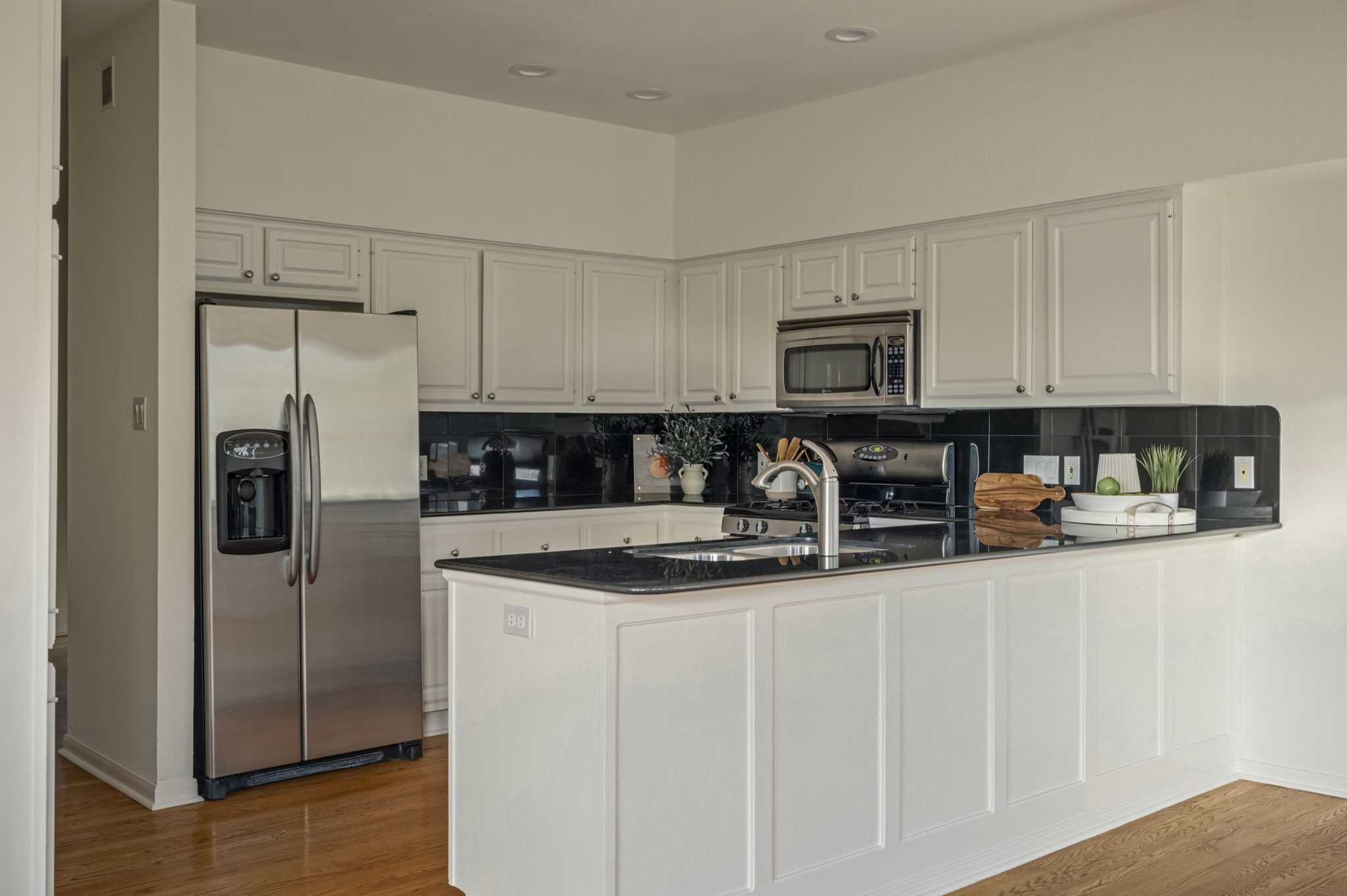6010 Long Champ Court, Unit 113 Austin, TX 78746 - Photo 15 of 25 Kitchen with tasteful backsplash, appliances with stainless steel finishes, a peninsula, white cabinets, and light wood-type flooring