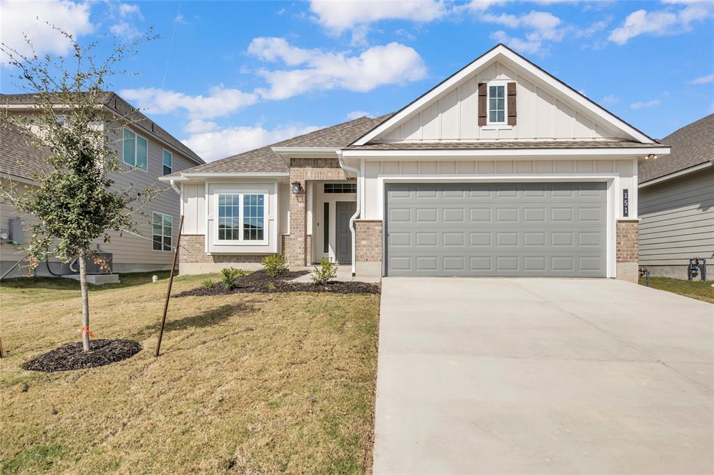 View of front of home with board and batten siding, brick siding, a front yard, concrete driveway, and an attached garage