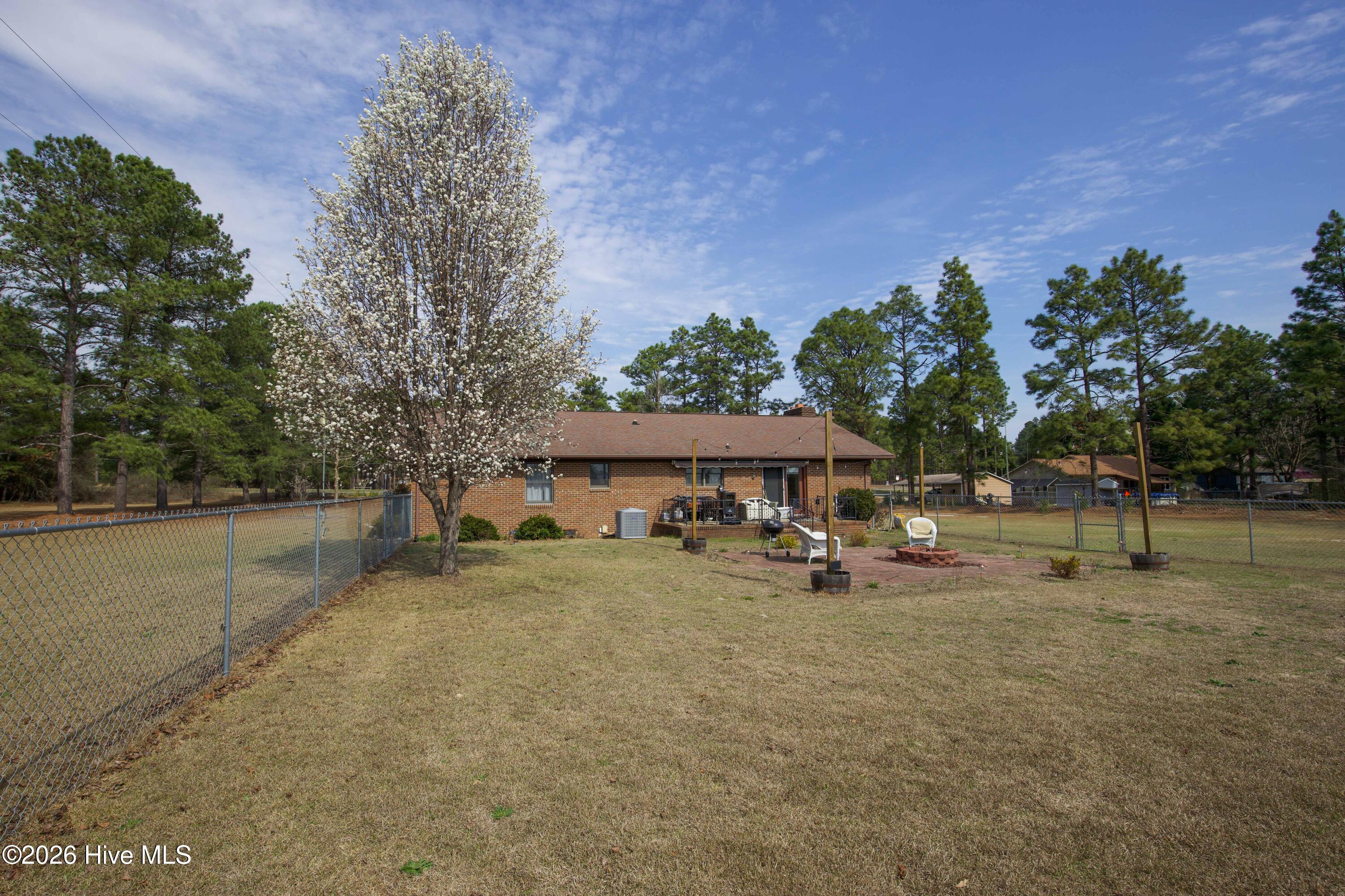 124 Joseph Road Aberdeen, NC 28315 - Photo 11 of 64 Rear view of the brick ranch home at 124 Joseph Road showing the backyard and outdoor gathering area. The spacious yard offers room for outdoor seating, gardening, and recreation while taking advantage of the approximately 5.06 acre property. Mature trees and open lawn create a private rural setting while still being conveniently located near Aberdeen, Southern Pines, Pinehurst, and commuter routes to Fort Bragg and Camp Mackall.