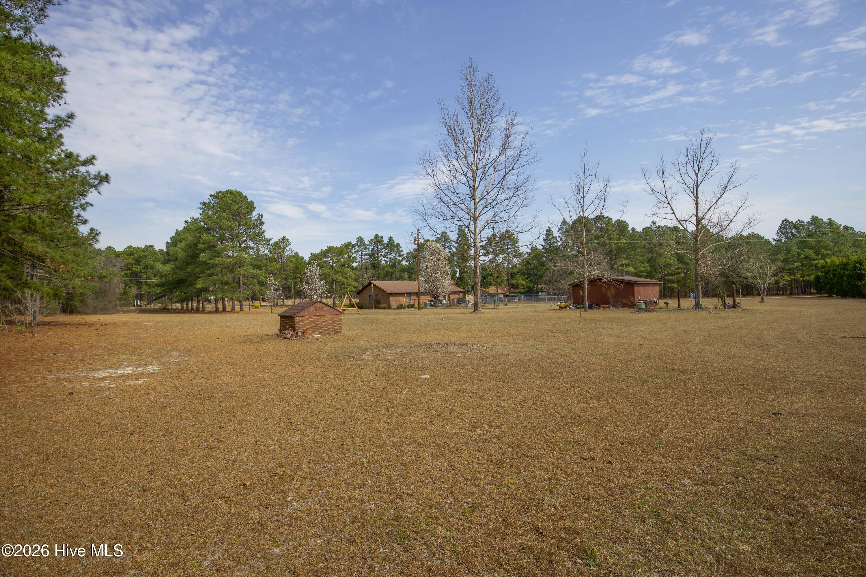 124 Joseph Road Aberdeen, NC 28315 - Photo 14 of 64 View across the open acreage at 124 Joseph Road showing the spacious yard and outbuildings located on the approximately 5.06 acre property. The land offers a combination of open lawn and mature trees that provide privacy and usable outdoor space. The detached buildings provide additional storage and workspace while the expansive yard offers room for recreation, gardening, or future improvements in a peaceful Moore County setting.