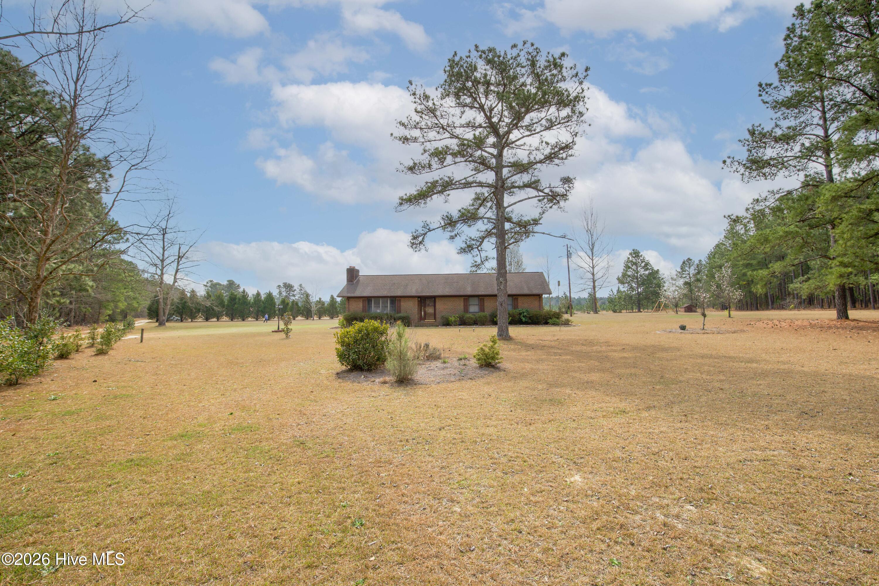 124 Joseph Road Aberdeen, NC 28315 - Photo 16 of 64 View across the open yard toward the brick ranch home at 124 Joseph Road. The property offers approximately 5.06 acres with a blend of open lawn and mature trees that provide space for outdoor recreation, gardening, or additional improvements. The home sits back from the road, creating a peaceful rural setting while remaining conveniently located near Aberdeen, Southern Pines, Pinehurst, and commuter routes to Fort Bragg and Camp Mackall.