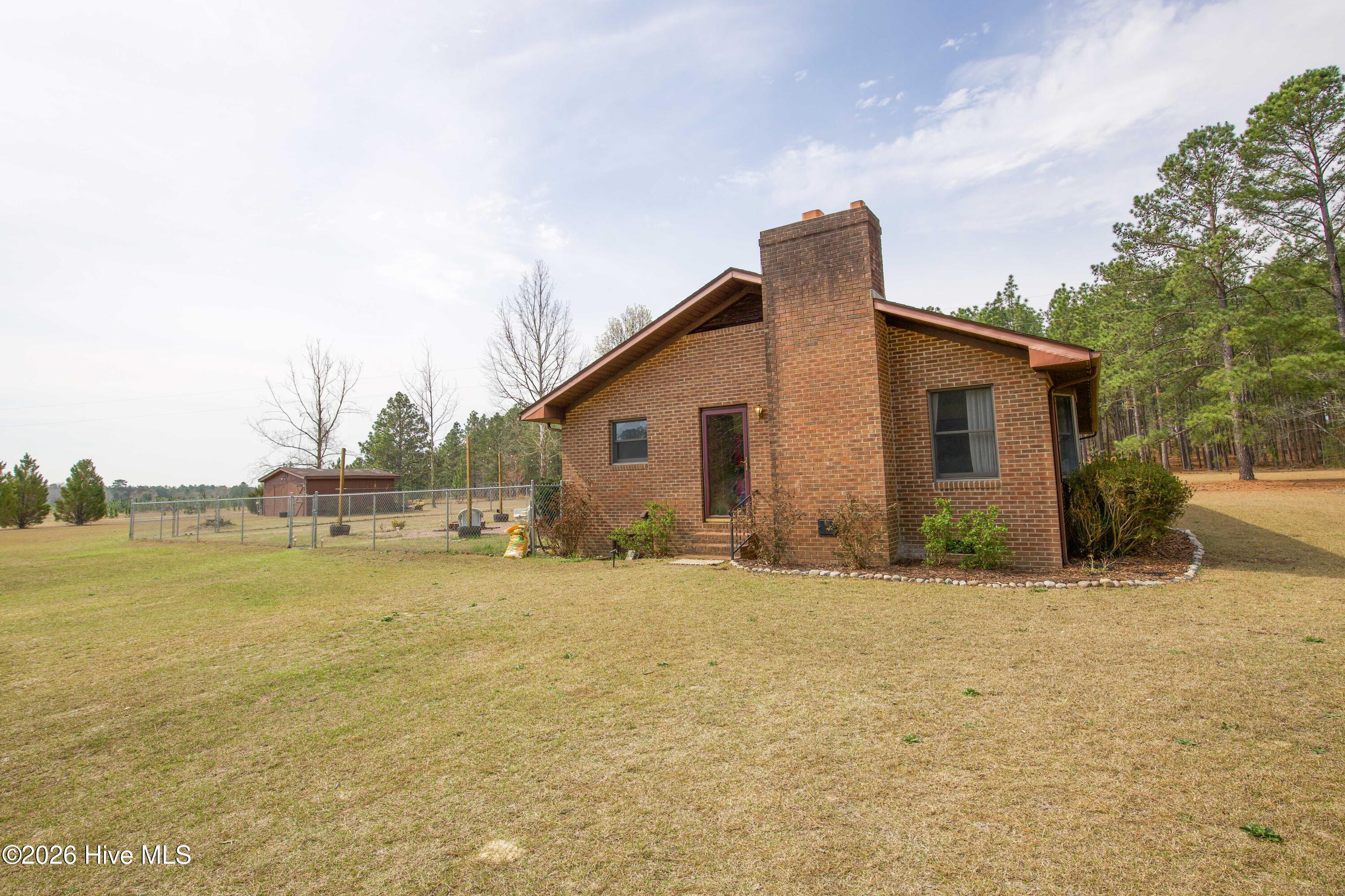 124 Joseph Road Aberdeen, NC 28315 - Photo 17 of 64 Side view of the brick ranch home at 124 Joseph Road showing the spacious yard and surrounding open land. The home sits on approximately 5.06 acres with a mix of lawn and mature trees that provide privacy and a peaceful rural setting. The expansive property offers plenty of space for outdoor activities, gardening, or additional improvements while remaining conveniently located near Aberdeen, Southern Pines, and Pinehurst.