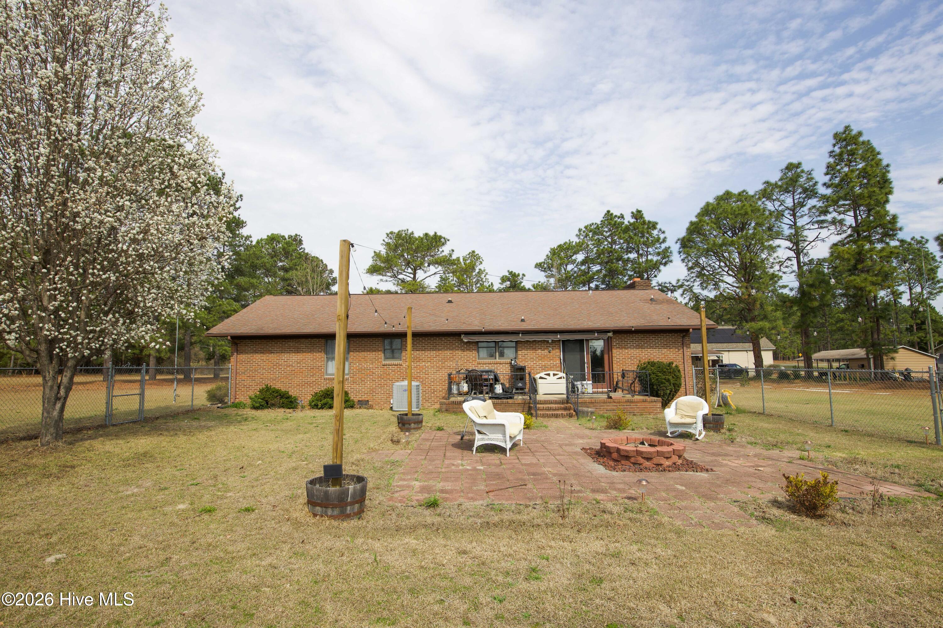 124 Joseph Road Aberdeen, NC 28315 - Photo 20 of 64 Rear view of the brick ranch home at 124 Joseph Road showing the backyard patio and outdoor seating area. The home sits on approximately 5.06 acres in Moore County with a combination of open lawn and mature trees. The backyard provides a comfortable setting for outdoor gatherings, relaxing by the firepit, or enjoying the quiet rural surroundings while still being conveniently located near Aberdeen, Southern Pines, and Pinehurst.