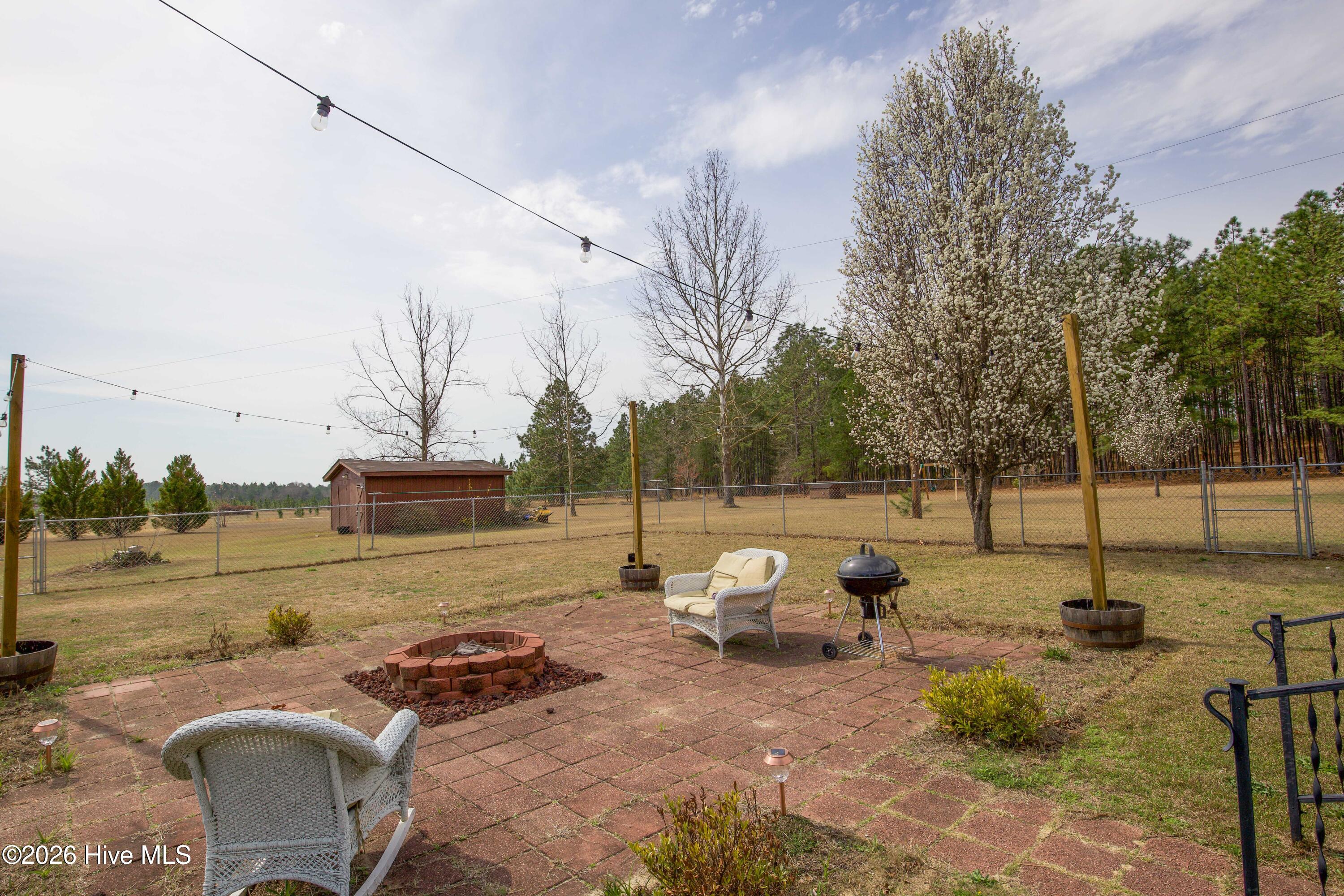 124 Joseph Road Aberdeen, NC 28315 - Photo 23 of 64 Backyard patio view at 124 Joseph Road looking toward the open yard and detached workshop in the distance. The property offers approximately 5.06 acres with a mix of open space and mature trees, providing room for recreation, gardening, and outdoor gatherings.