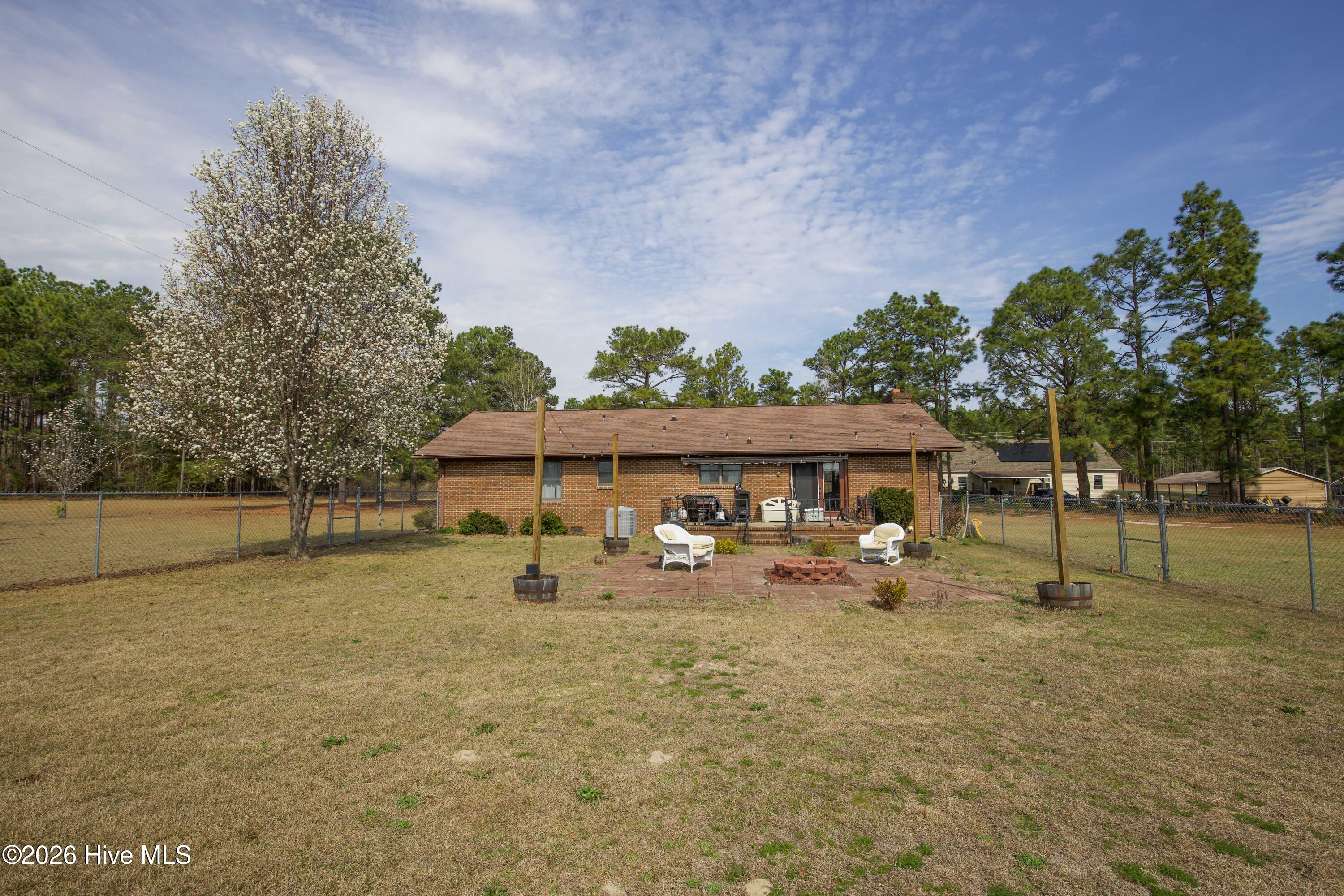 124 Joseph Road Aberdeen, NC 28315 - Photo 36 of 59 Rear view of the brick ranch home at 124 Joseph Road showing the backyard and outdoor gathering area. The spacious yard provides plenty of room for outdoor seating, gardening, or recreation while enjoying the privacy of approximately 5.06 acres in Moore County. Mature trees surround the property and help create a quiet rural setting. The open lawn offers flexibility for outdoor activities while remaining conveniently located near Aberdeen, Southern Pines, Pinehurst, and commuter routes to Fort Bragg and Camp Mackall.