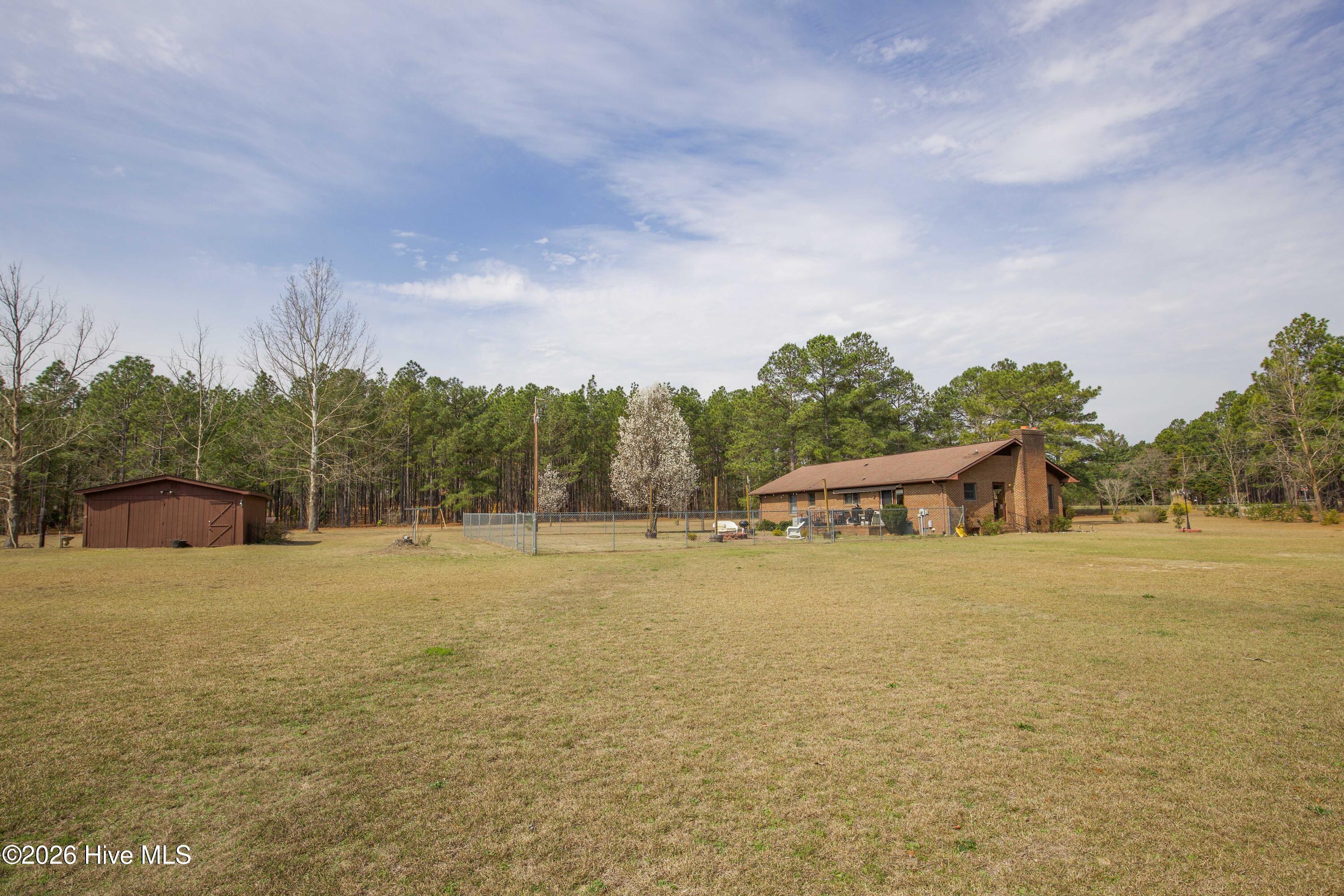 124 Joseph Road Aberdeen, NC 28315 - Photo 40 of 59 View across the backyard of 124 Joseph Road showing the open yard space located on the approximately 5.06 acre property. The smaller building visible in the distance is the powered workshop, providing space for tools, hobbies, equipment storage, or small business use. The large open lawn offers room for outdoor activities, gardening, or additional improvements while enjoying the privacy of a rural Moore County setting.