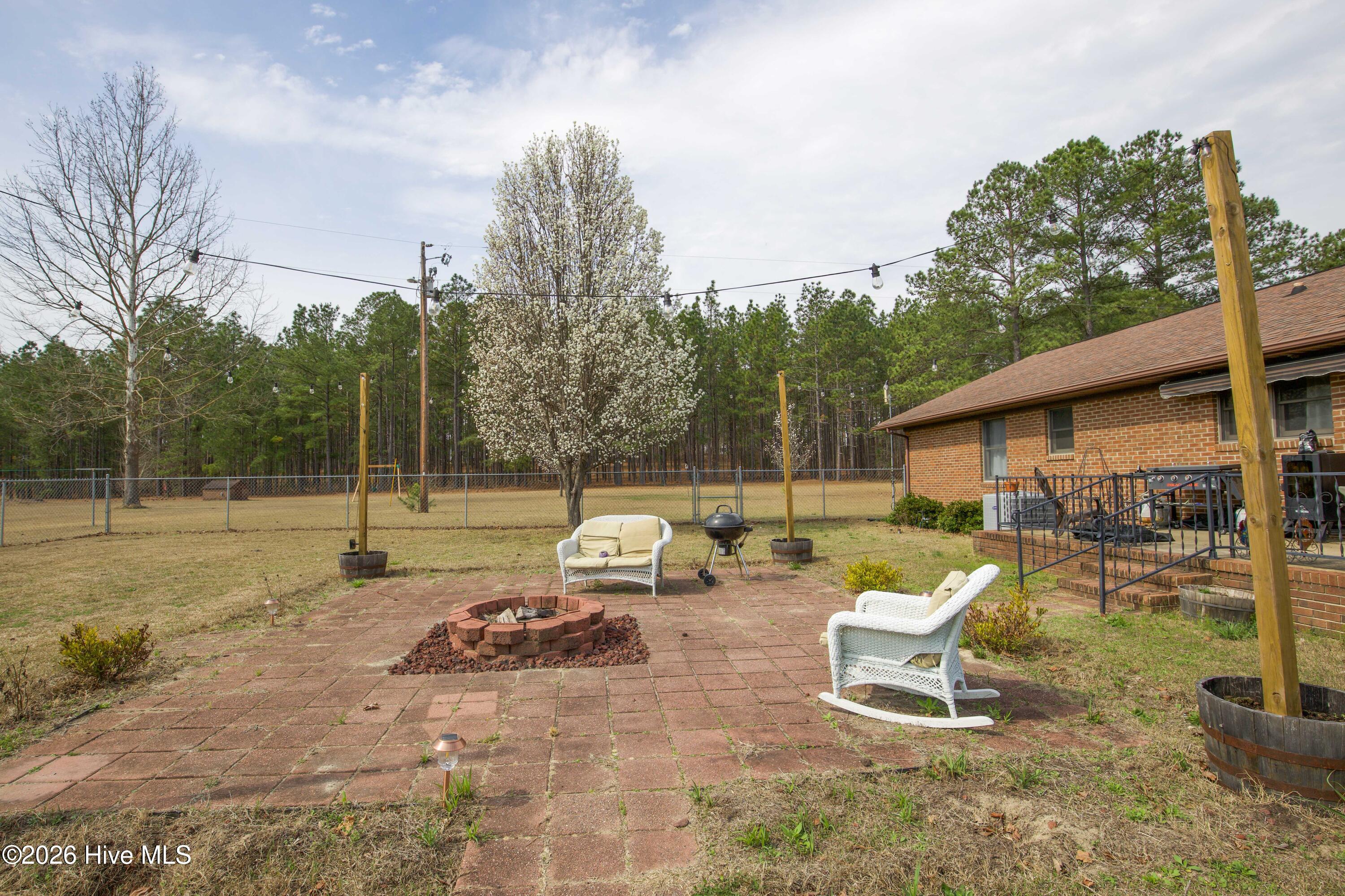 124 Joseph Road Aberdeen, NC 28315 - Photo 48 of 59 Backyard patio area at 124 Joseph Road providing a space for outdoor seating, grilling, or relaxing while enjoying the open yard and surrounding acreage. The approximately 5.06 acre property offers a quiet rural setting with room for gardening, recreation, and outdoor gatherings. Mature trees and open lawn create a private environment while remaining conveniently located near Aberdeen, Southern Pines, Pinehurst, and commuter routes to Fort Bragg and Camp Mackall.