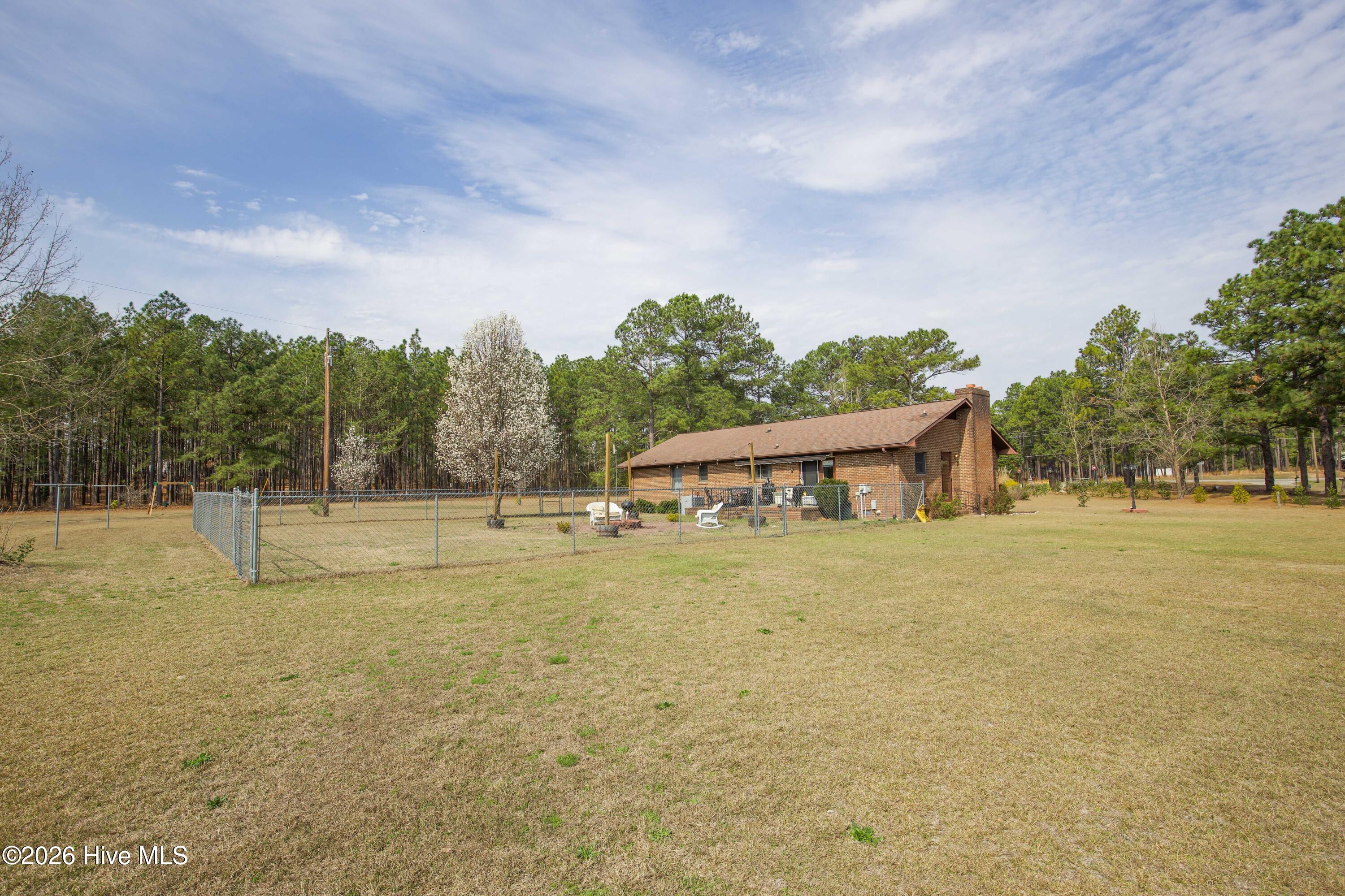 124 Joseph Road Aberdeen, NC 28315 - Photo 7 of 64 Rear view of the home and backyard at 124 Joseph Road showing the open yard and fenced area behind the house. The property sits on approximately 5.06 acres with a combination of open lawn and mature trees that provide privacy and usable outdoor space. The expansive yard offers flexibility for gardening, recreation, pets, or future outdoor improvements.