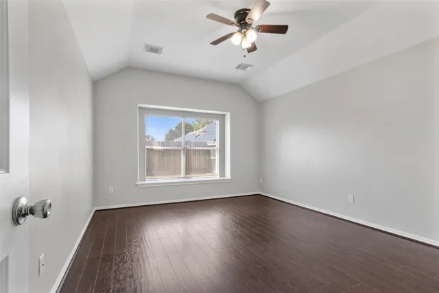 an empty room with wooden floor chandelier fan and windows