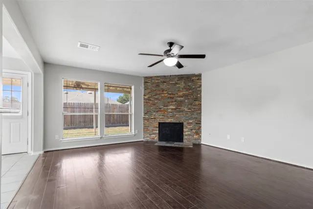 an empty room with wooden floor fireplace and windows
