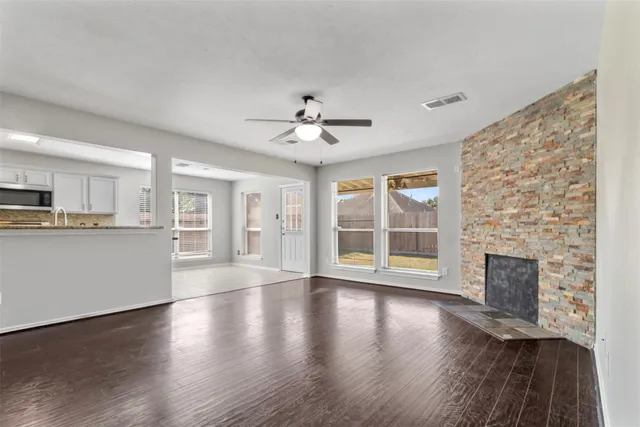 a view of an empty room with wooden floor and a kitchen