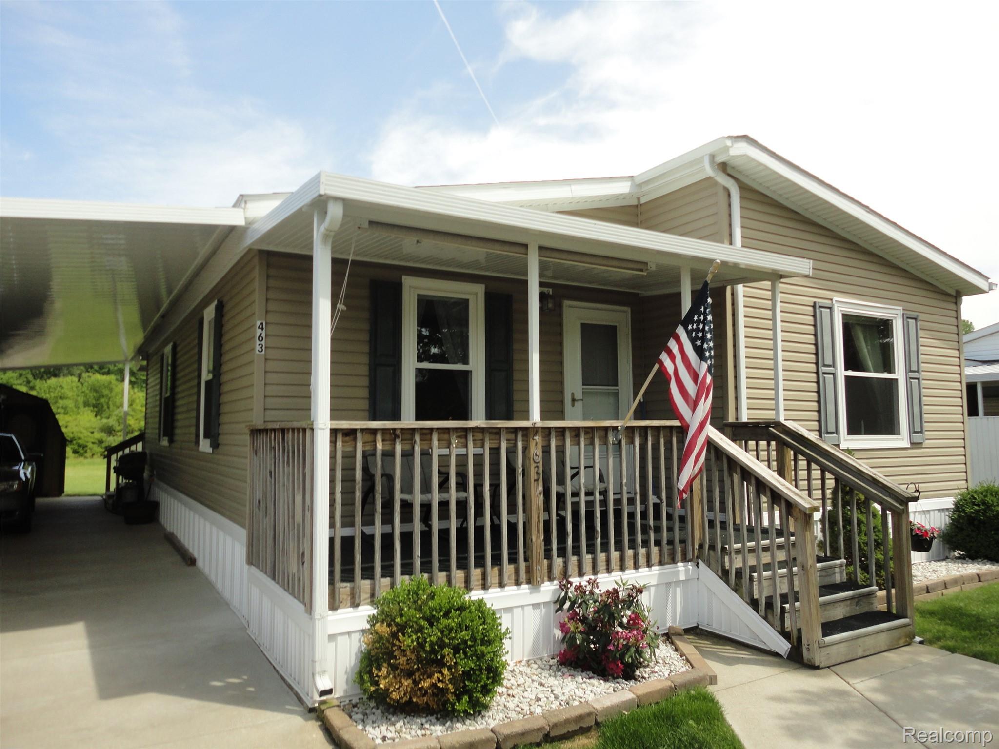 463 Edinborough Temperance, MI 48182 - Photo 15 of 23 Exterior featuring tan siding, a covered front porch with wood railings, a concrete driveway leading to a car port, and foundation skirting