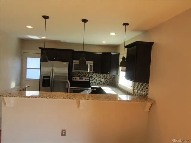 a kitchen with stainless steel appliances kitchen island granite countertop a refrigerator a oven and a wooden floor