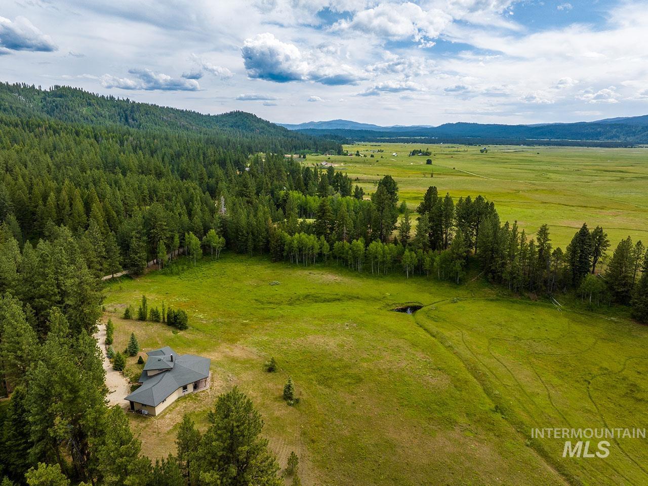 10885 Callender Road Cascade, ID 83611 - Photo 1 of 1 Extensive green landscape surrounding a single-story property with a dark shingled roof, bordered by a dense forest