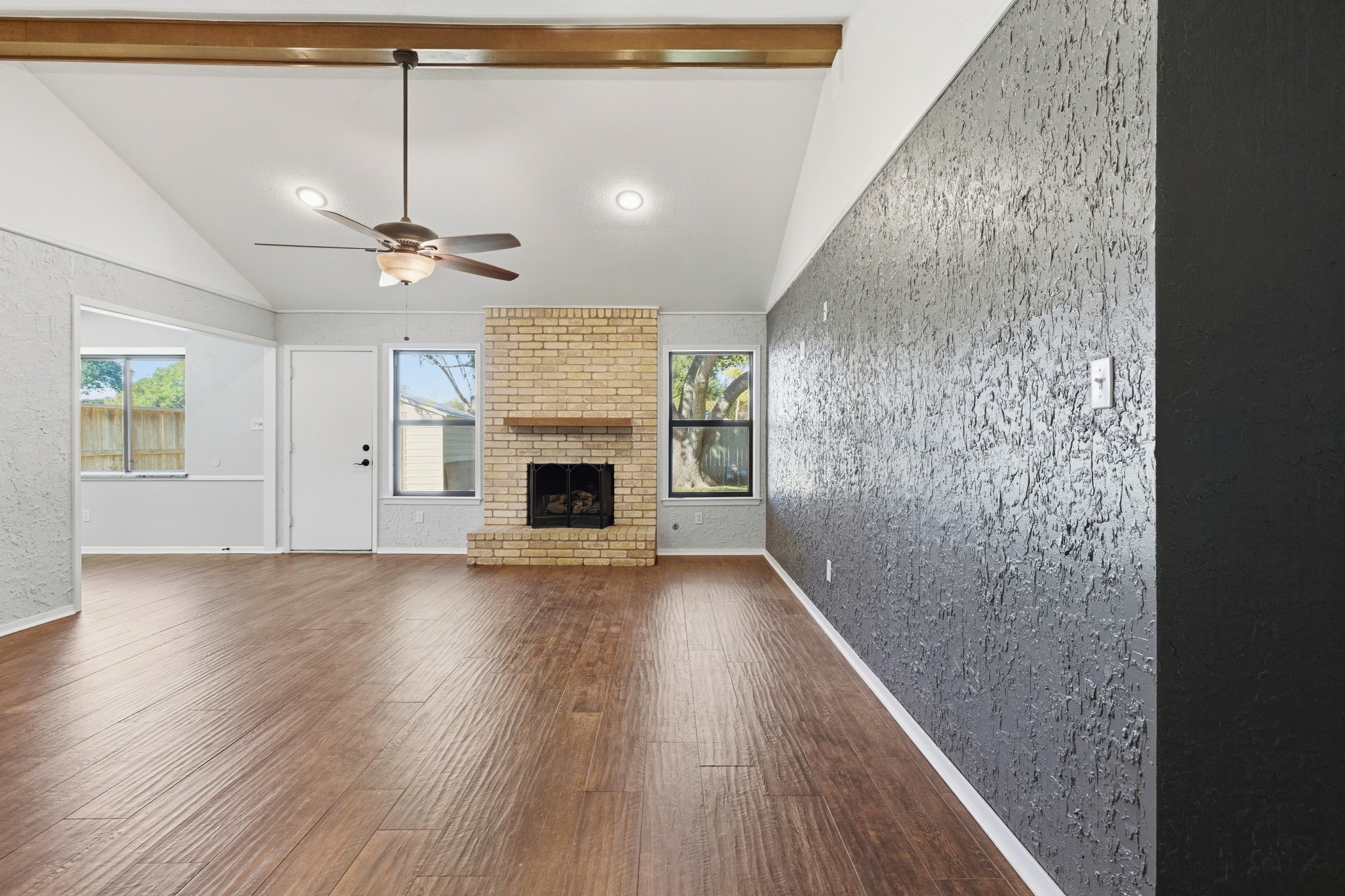 3721 Avenue R Rosenberg, TX 77471 - Photo 1 of 43 Spacious living room with vaulted ceiling, exposed beam detail, wood-look tile flooring, and a brick fireplace flanked by windows for natural light.