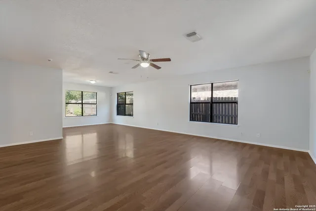 a view of an empty room with wooden floor and a ceiling fan