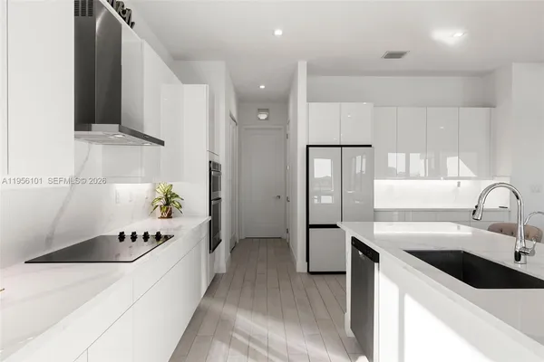 a large kitchen with a sink dishwasher a refrigerator and cabinets with wooden floor