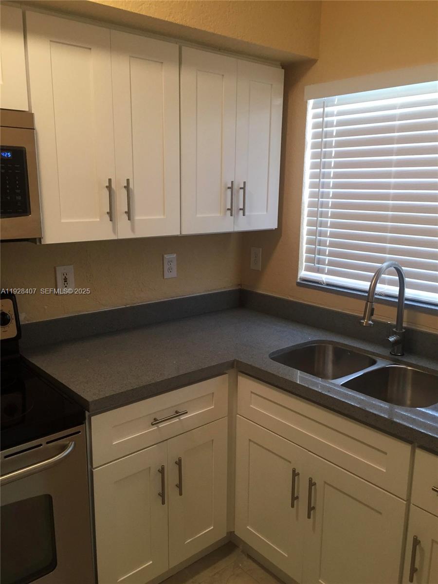 457 Northwest 84th Street, Unit 457 Miami, FL 33150 - Photo 3 of 4 a kitchen with granite countertop white cabinets and a sink