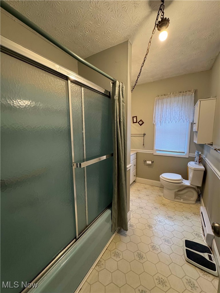 8631 Center Road Ashtabula, OH 44004 - Photo 19 of 25 Bathroom featuring bath / shower combo with glass door, toilet, a textured ceiling, baseboards, and tile patterned floors