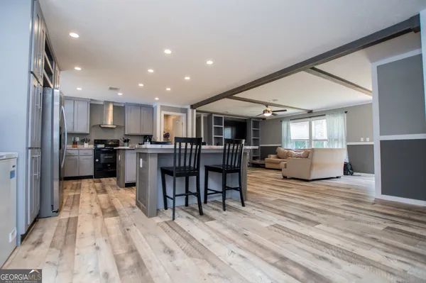 a living room with stainless steel appliances furniture wooden floor and a kitchen view