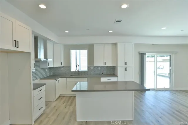 a large kitchen with stainless steel appliances granite countertop a stove a sink a refrigerator and white cabinets with wooden floor