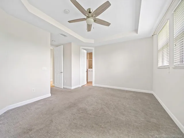 an empty room with chandelier fan and windows