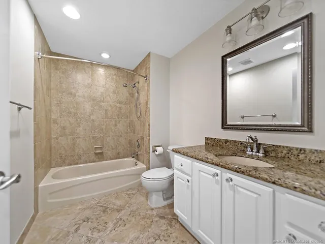 a bathroom with a granite countertop sink mirror vanity bathtub and a toilet