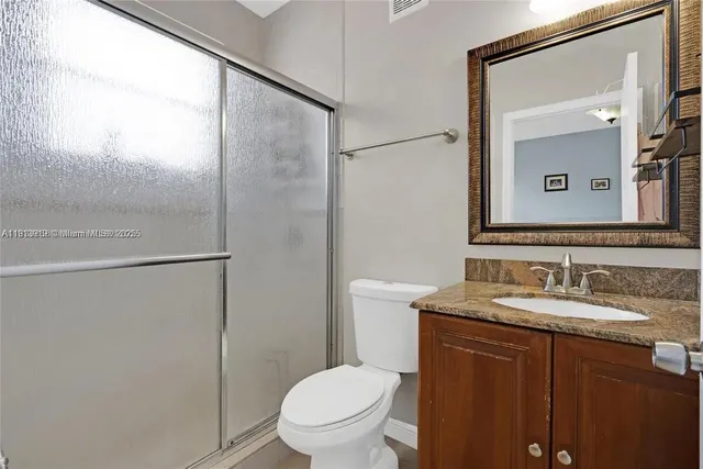 a bathroom with a granite countertop sink toilet mirror and a shower