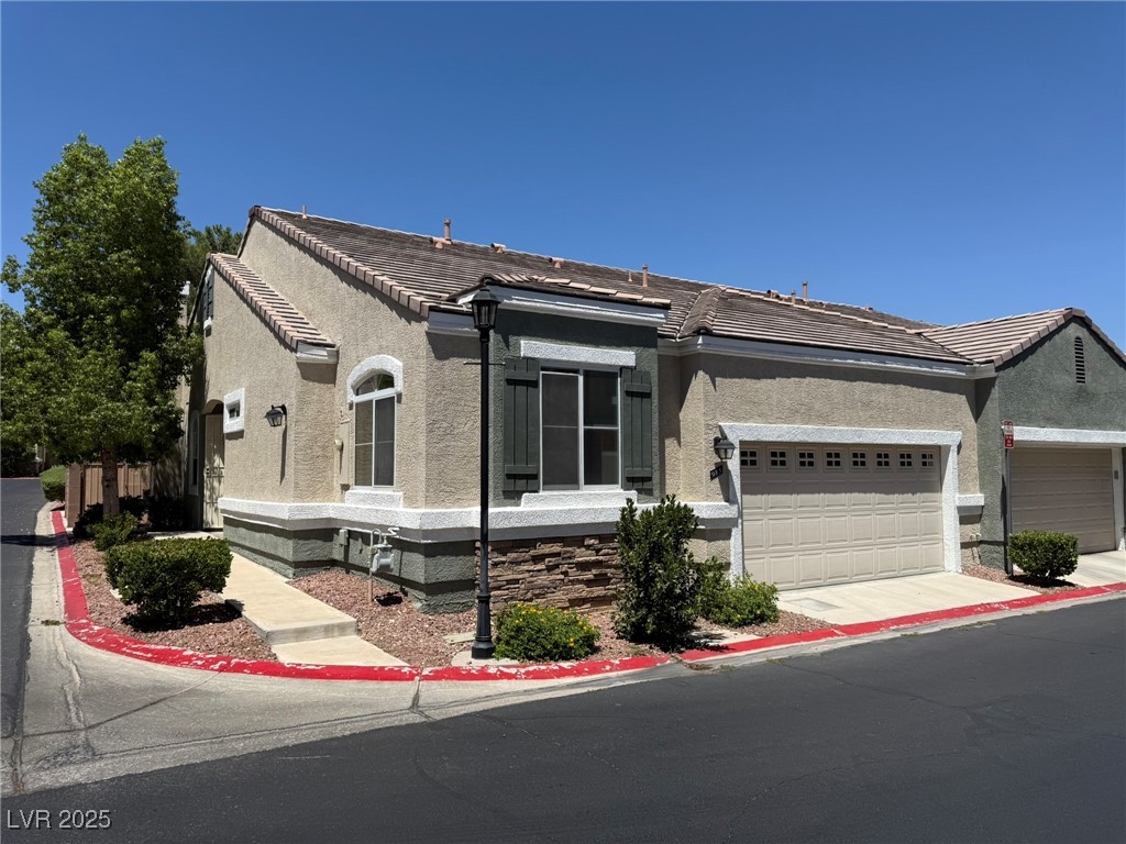 View of front of property with an attached garage, stucco siding, a tile roof, and driveway