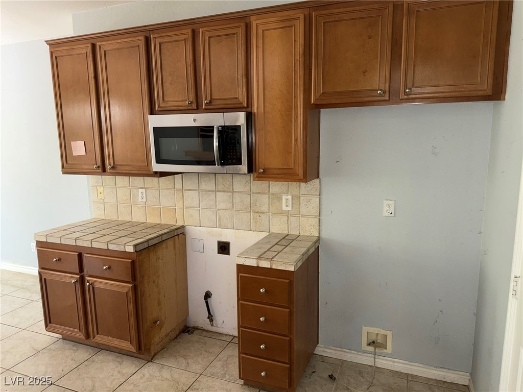 985 Prestwick Street Las Vegas, NV 89145 - Photo 21 of 27 Kitchen featuring tasteful backsplash, brown cabinetry, stainless steel microwave, and tile countertops