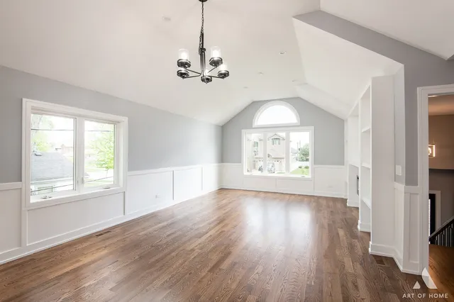 an empty room with wooden floor chandelier and windows