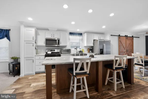 a kitchen with stainless steel appliances granite countertop a stove a sink a microwave a refrigerator and white cabinets with wooden floor