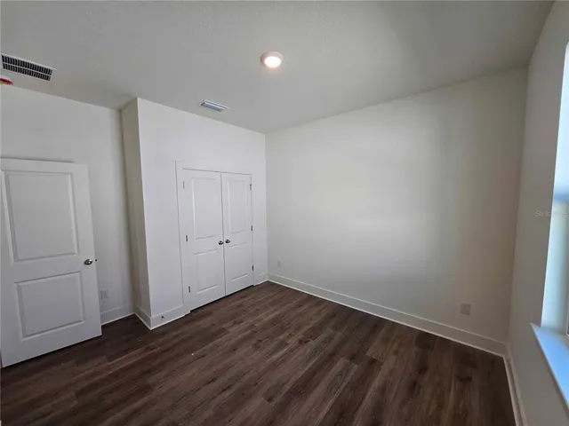 a view of an empty room with wooden floor and closet