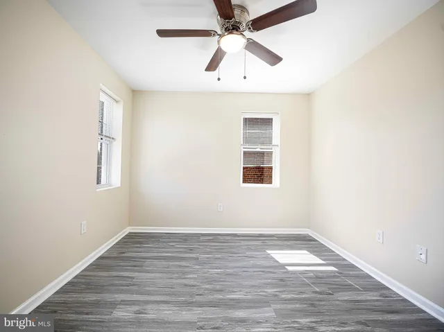 an empty room with wooden floor ceiling fan and windows