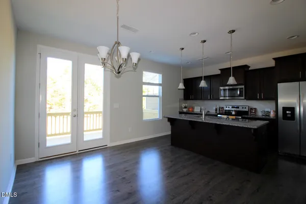 a kitchen with stainless steel appliances granite countertop a refrigerator a sink dishwasher a stove and a dining table with wooden floor