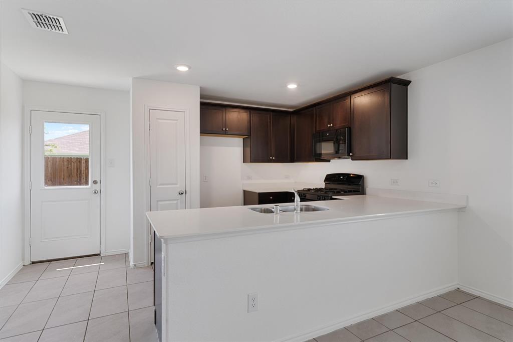 7781 Ruellia Road McKinney, TX 75071 - Photo 9 of 25 Kitchen featuring a peninsula, light countertops, dark brown cabinets, light tile patterned floors, and black appliances