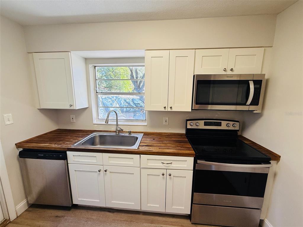 3818 Northeast 13th Drive Gainesville, FL 32609 - Photo 6 of 12 a kitchen with white cabinets a sink and a stove with wooden floor