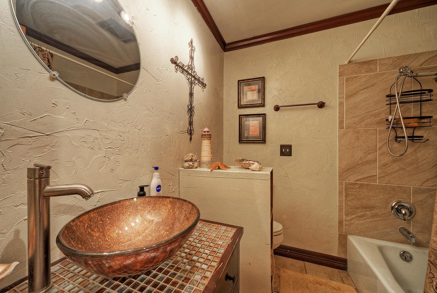 2300 Robin Road Manchaca, TX 78652 - Photo 19 of 36 A vessel sink rests on a mosaic tile countertop beside a tiled tub shower.