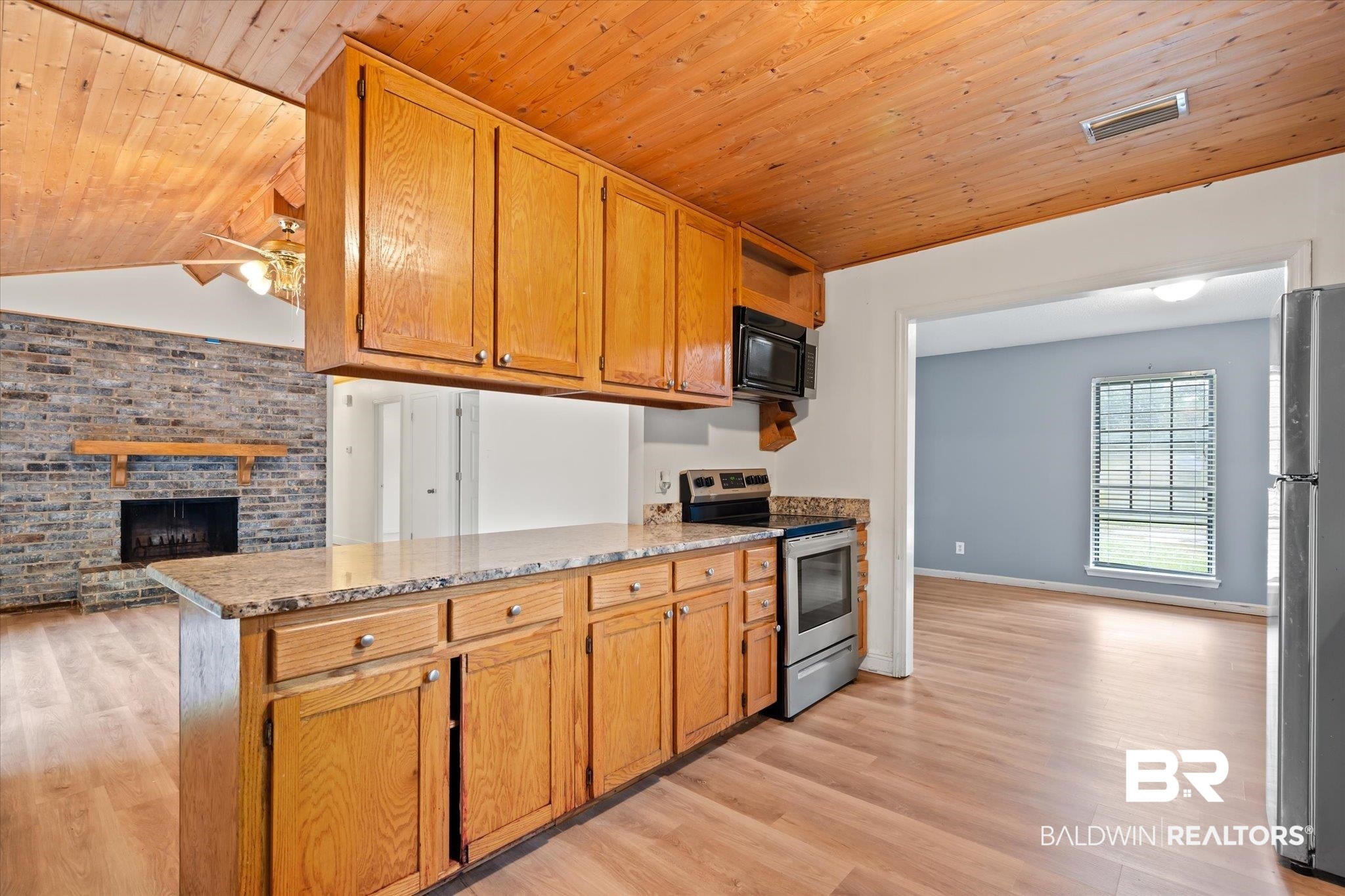 9445 Howells Ferry Road Semmes, AL 36575 - Photo 6 of 20 Kitchen with a fireplace, light wood-type flooring, appliances with stainless steel finishes, vaulted ceiling, and kitchen peninsula