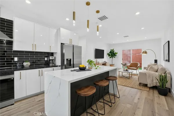 a kitchen with stainless steel appliances kitchen island granite countertop a stove a sink a refrigerator and white cabinets with wooden floor