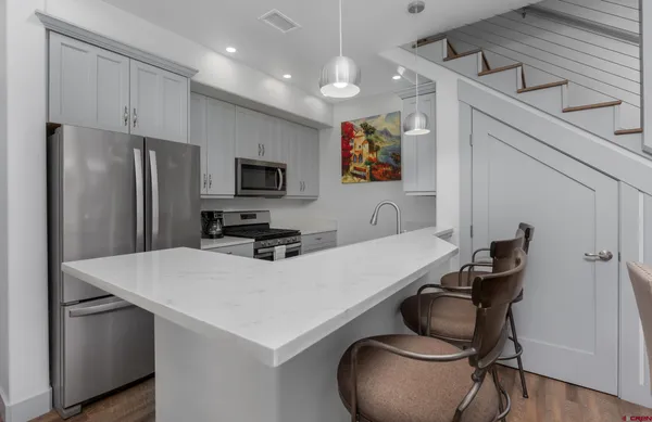 a kitchen with stainless steel appliances a refrigerator a stove a sink a dining table and chairs with wooden floor