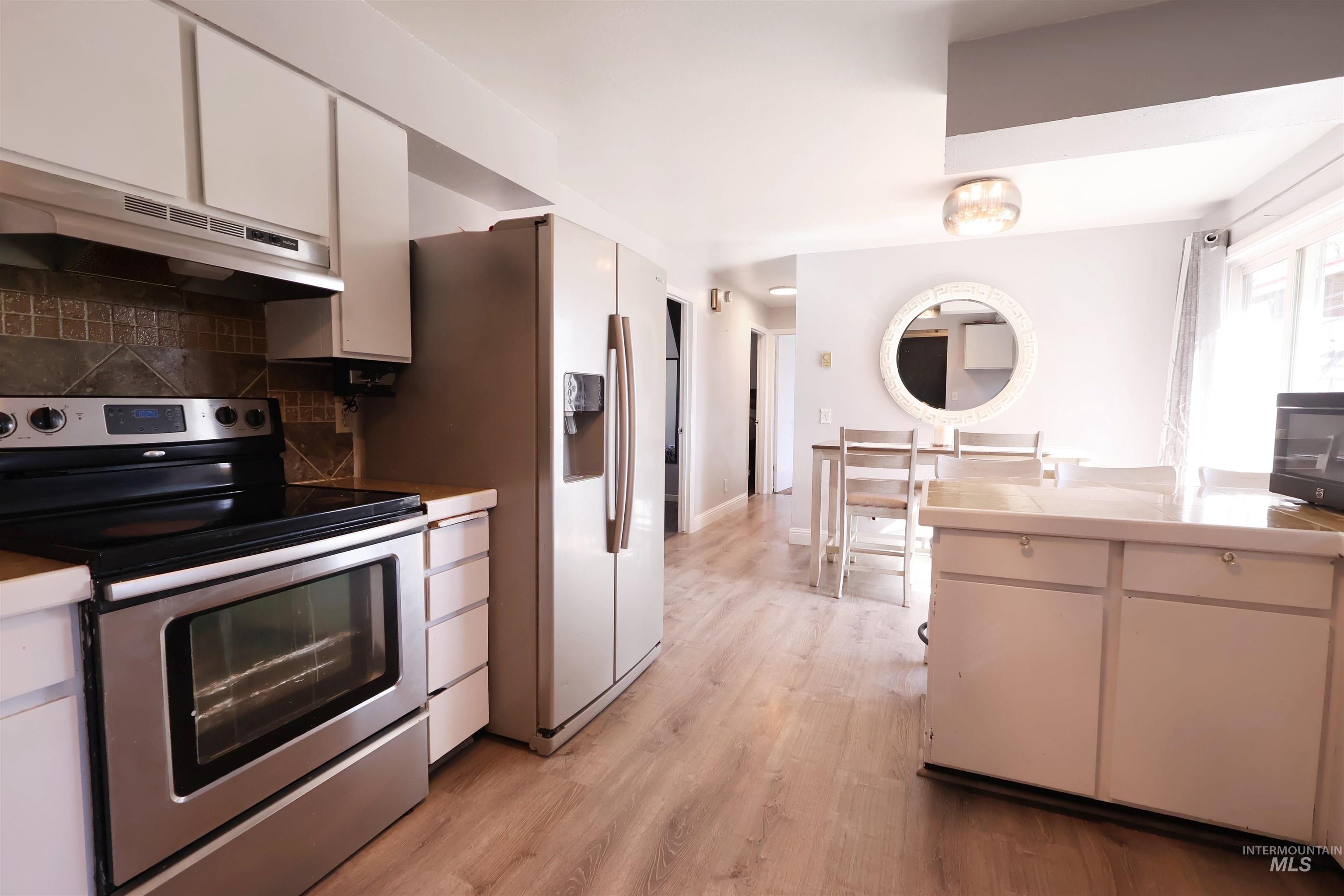 412 Linden Street Rupert, ID 83350 - Photo 7 of 17 Kitchen featuring stainless steel range with electric stovetop, white cabinetry, light wood-style floors, decorative backsplash, and light countertops