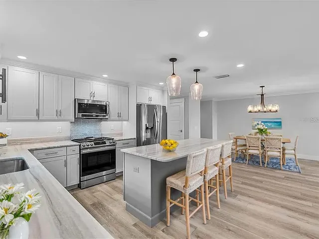 a kitchen with stainless steel appliances kitchen island granite countertop a stove a sink a refrigerator a microwave oven a dining table and chairs with wooden floor